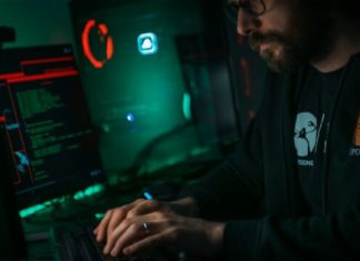 Will Cybersecurity Be Replaced by AI? A person in a dark room on a computer trying to figure out will cybersecurity be replaced by ai