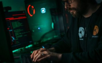 Will Cybersecurity Be Replaced by AI? A person in a dark room on a computer trying to figure out will cybersecurity be replaced by ai