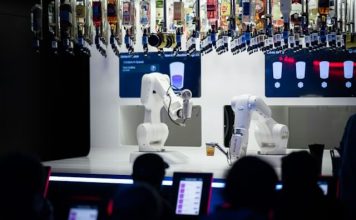 Business Process Automation vs Robotic Process Automation an image of business people looking at a robotic arm preparing drinks, which is to improve the business process automation cycle