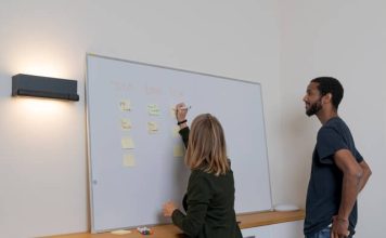 Best Capacity Planning Software in 2025 2 people discussing the Best Capacity Planning Software by using a white board and sticky notes